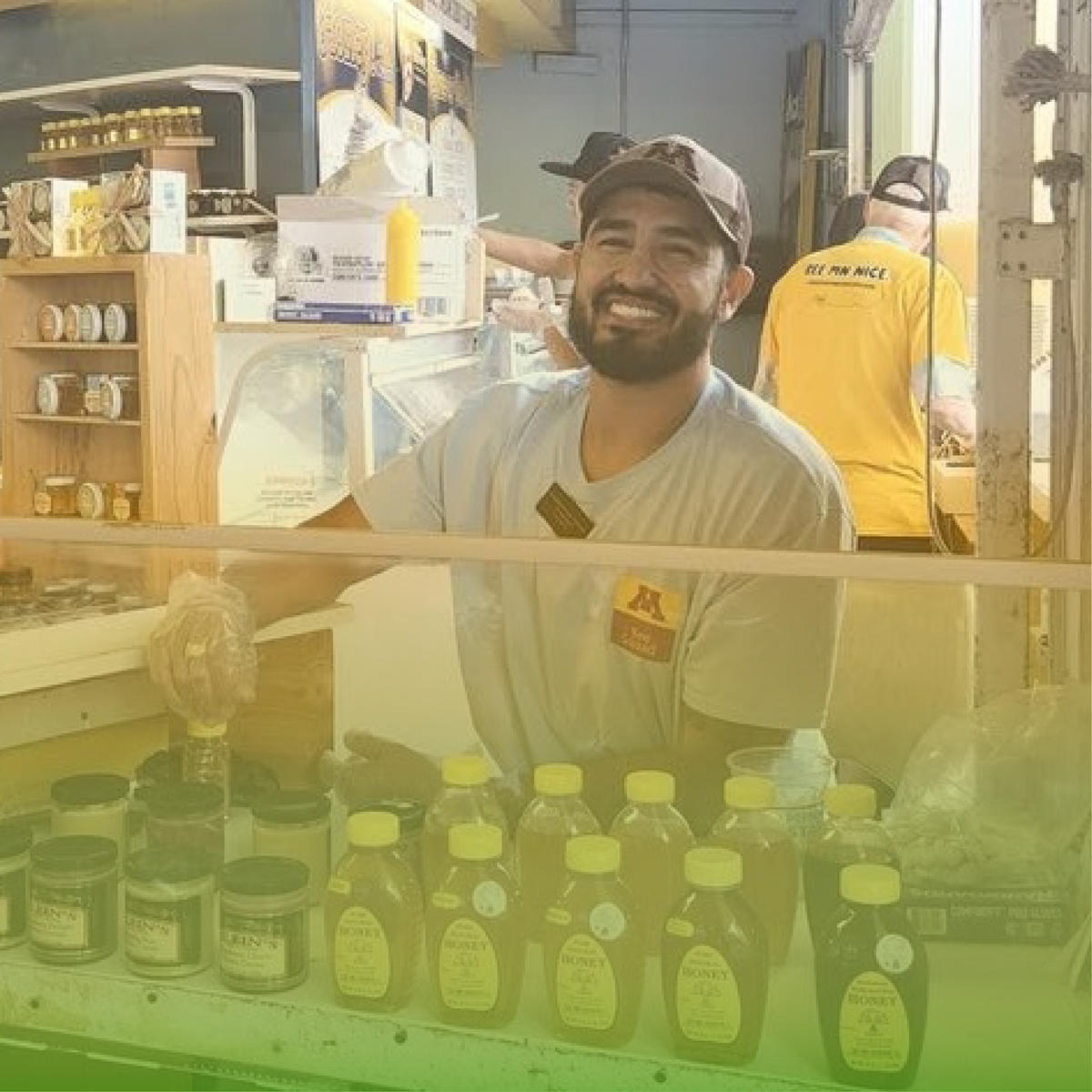 Image of someone smiling behind a row of bottled honey.