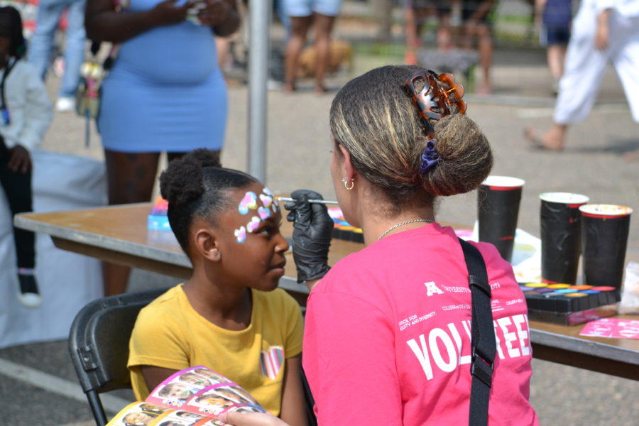 Image of a young black girl having her face painted by a Juneteenth volunteer.
